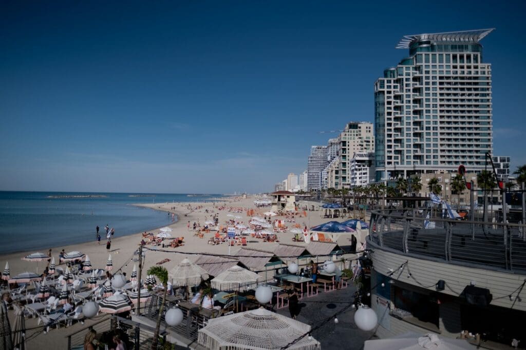 Foto di Levi Meir Clancy una spiaggia affollata a Tel Aviv con appartamenti di lusso immobiliari vicino alla spiaggia con ombrelloni ed edifici sullo sfondo