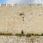 Dos personas caminando junto al muro de las lamentaciones de ladrillo beige, la ley de sucesión y sucesiones de Israel de 1965